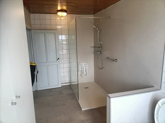 Ruime badkamer met inloopdouche, glazen wand, crème wandpanelen, opklapzitje en steunbeugel