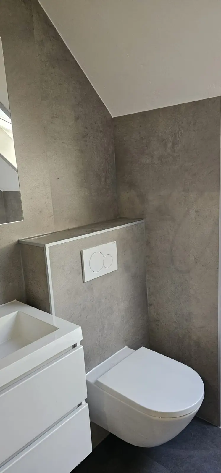 Stijlvolle, gerenoveerde badkamer met grijze wanden, zwevend toilet en witte wastafel met meubel. Schoon en modern design.