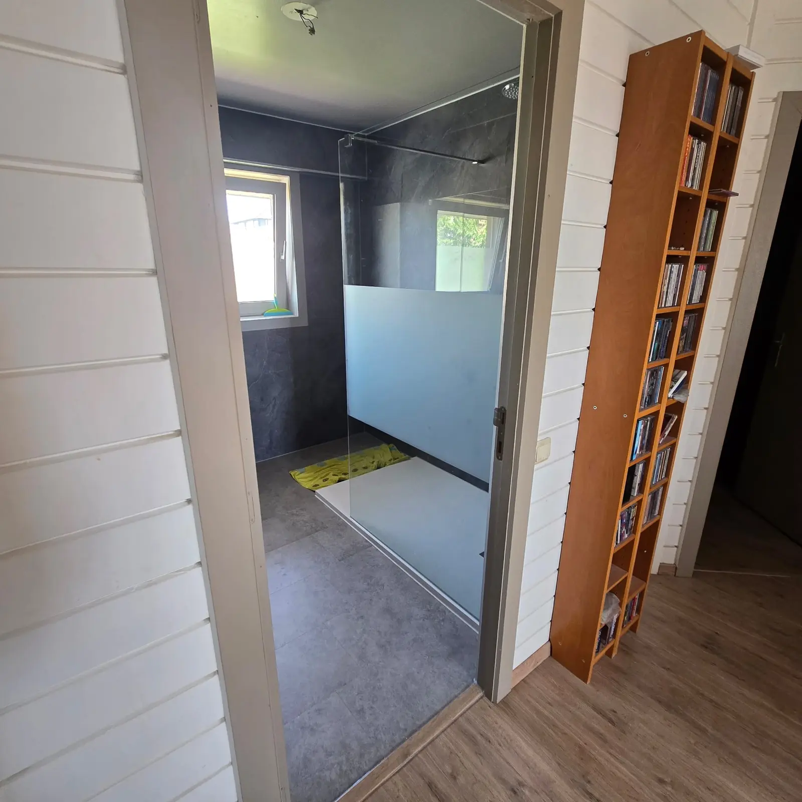 Overzicht van een moderne badkamer met drempelloze inloopdouche en donkere wandtegels, gezien vanuit de deuropening.