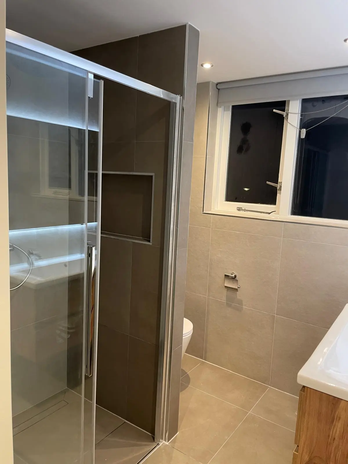 Gerenoveerde badkamer met ruime inloopdouche, modern toilet en wastafelmeubel, voorzien van lichte tegels en spotverlichting.