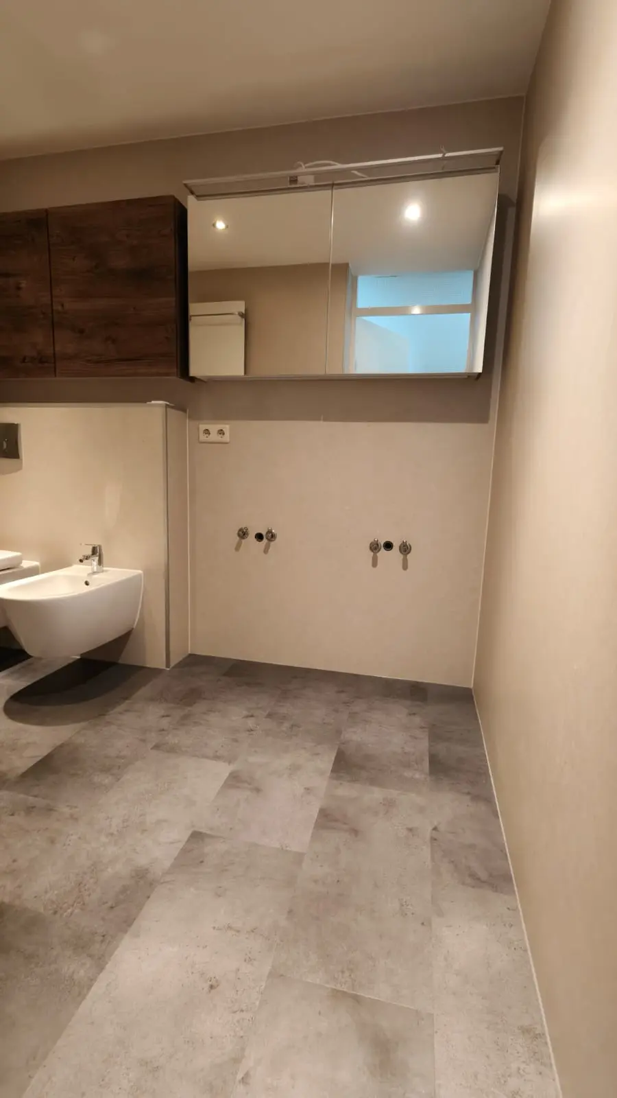 Nieuw gerenoveerde badkamer met grijze vloertegels, lichte wanden, spiegelkast en voorbereiding voor dubbele wastafel en toilet.