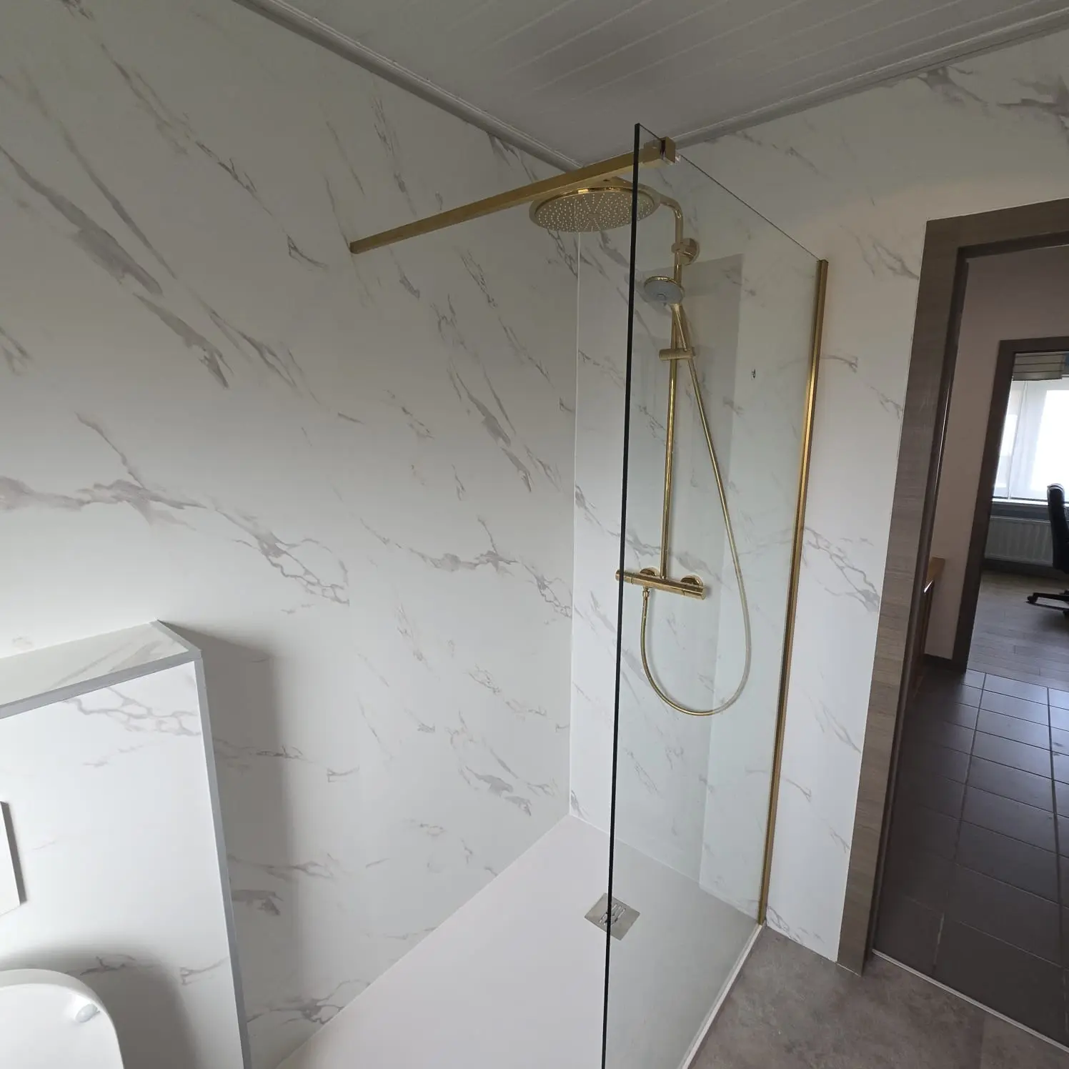 moderne badkamer met drempelloze inloopdouche, witte marmerlook wandpanelen en gouden douchekranen.